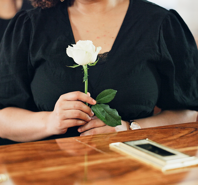 a woman laying down a white rose on top of a coffin